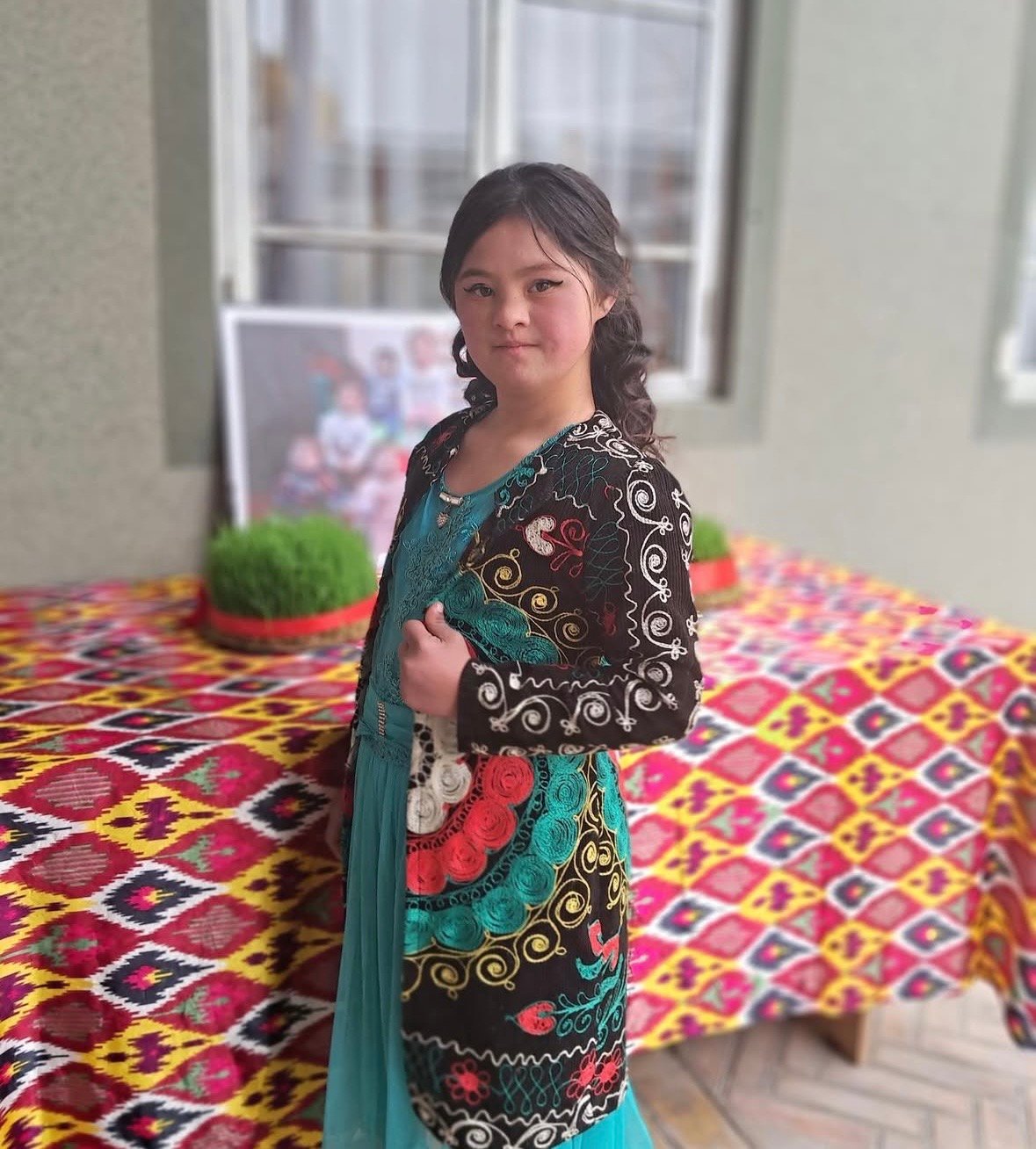 A girl with Down syndrome in an embroidered traditional jacket beside a Navruz table
